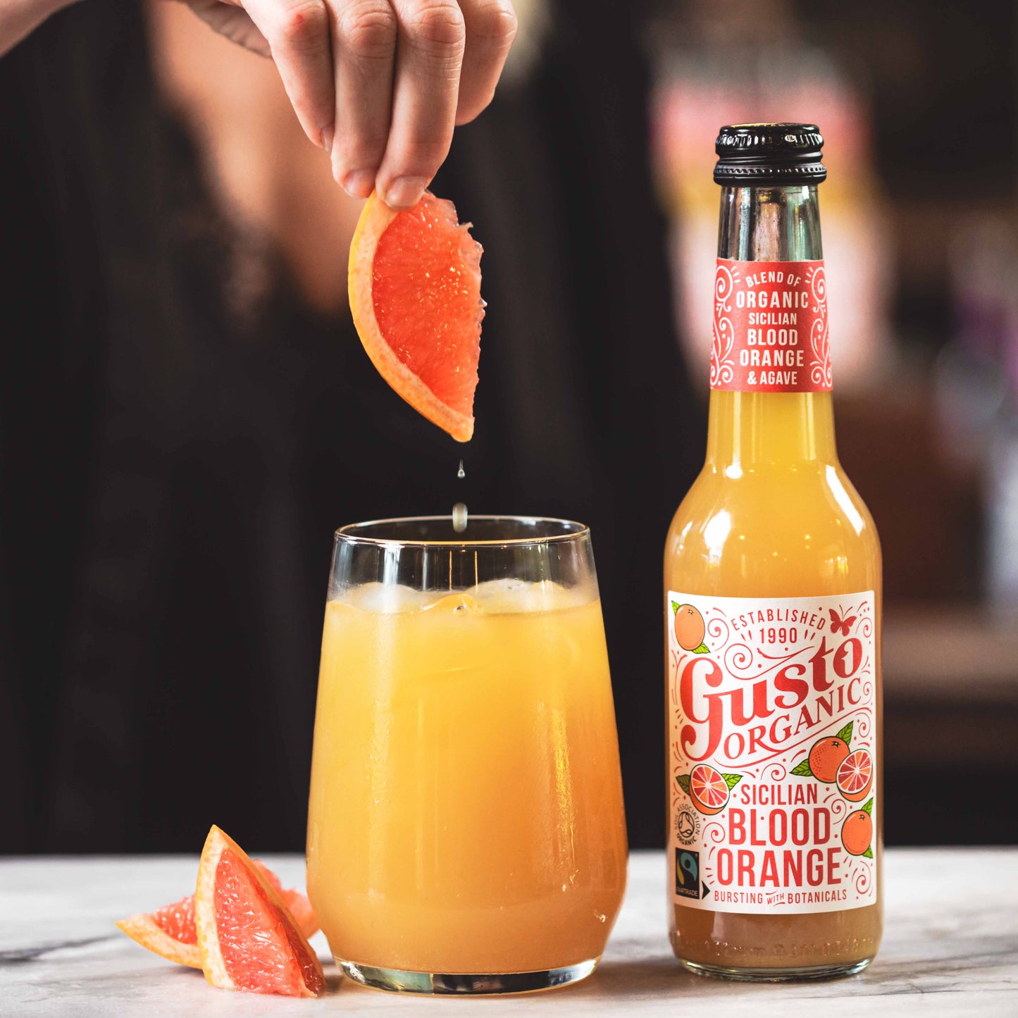 Bottle of Fairtrade Gusto Organic Sicilian Blood Orange with a Great Taste award in a glass next to an unopened bottle.
