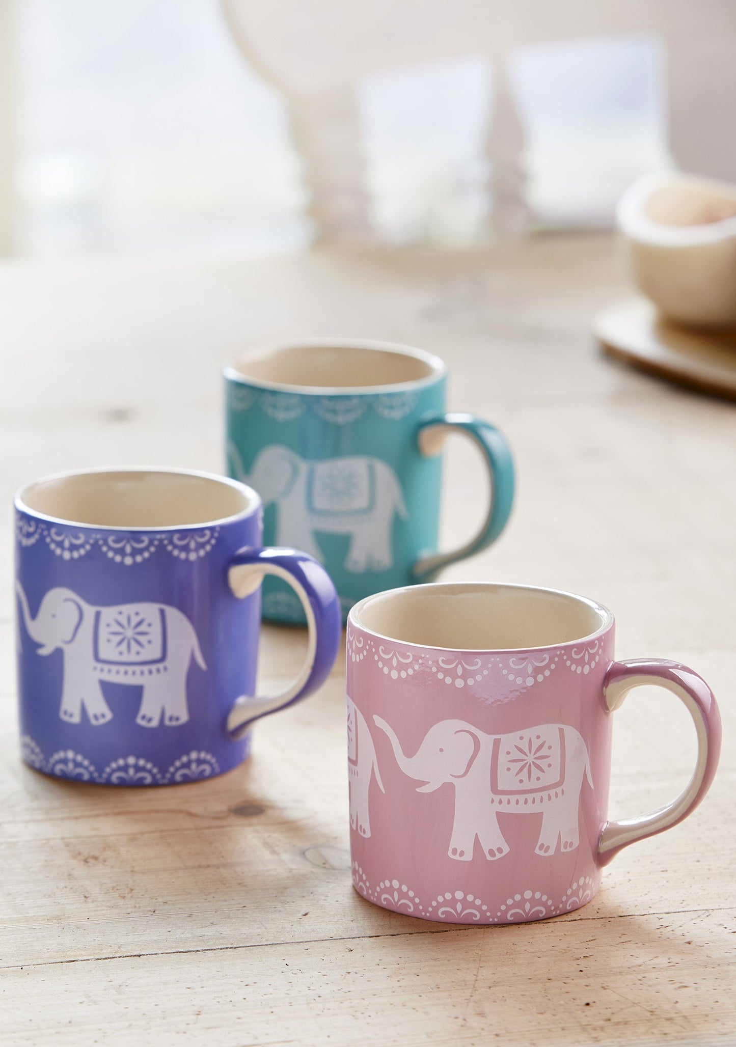 Three mugs with an elephant design. There is a blue, purple and pink mug with a white elephant on each.