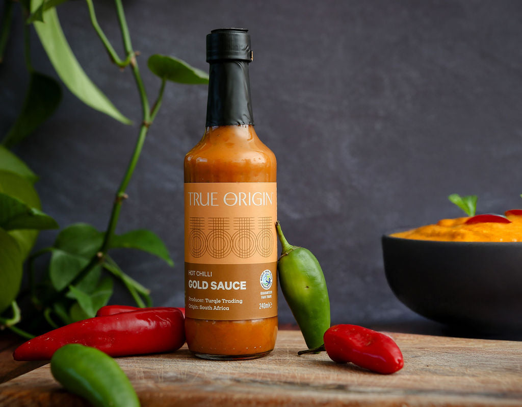 Bottle of True Origin hot chilli gold sauce with peppers on a wooden surface