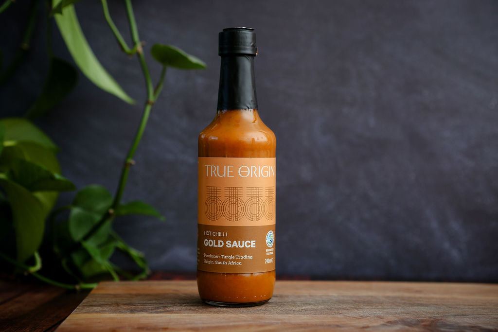 Bottle of True Orgin Gold Sauce on a wooden surface with a dark background