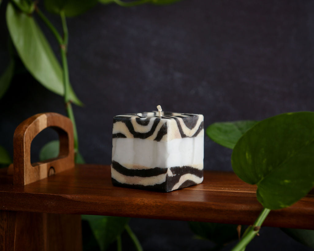 Zebra-patterned candle on a wooden surface with a dark background and green leaves.