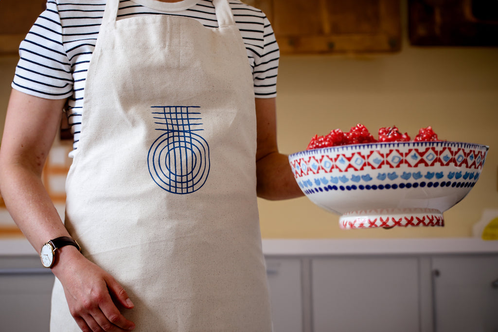 A woman carrying a bowl of raspberries wearing a beige Fairtrade cotton apron with the True Origin logo on the front.