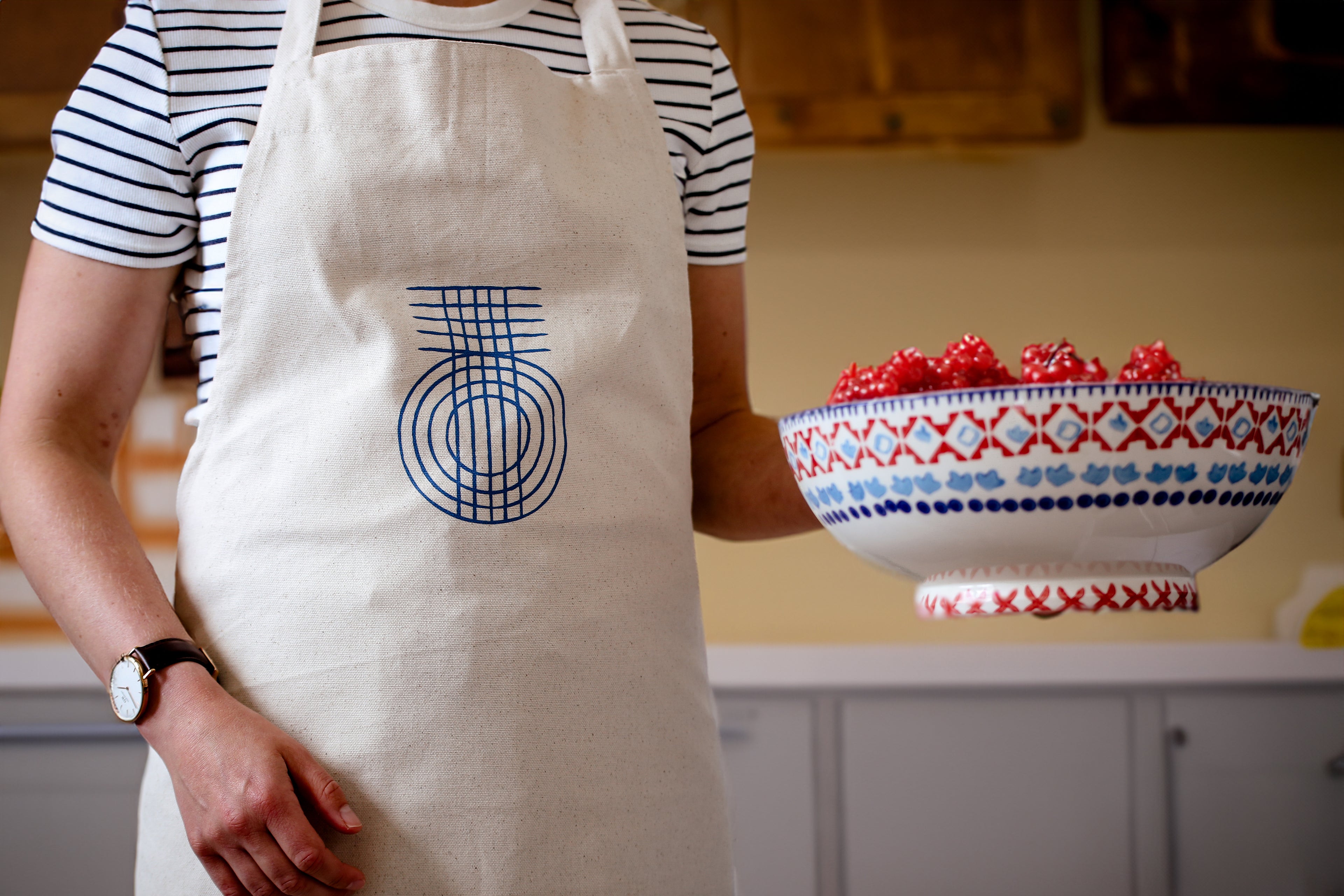 A woman carrying a bowl of raspberries wearing a beige Fairtrade cotton apron with the True Origin logo on the front.