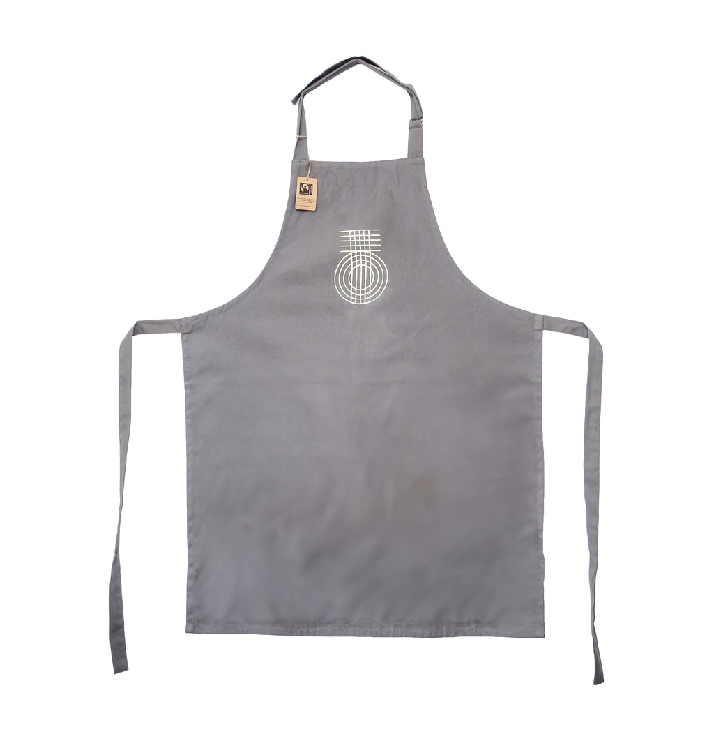 A grey apron with a printed True Origin logo on the front, featuring adjustable neck and waist ties.  Made with Fairtrade cotton.