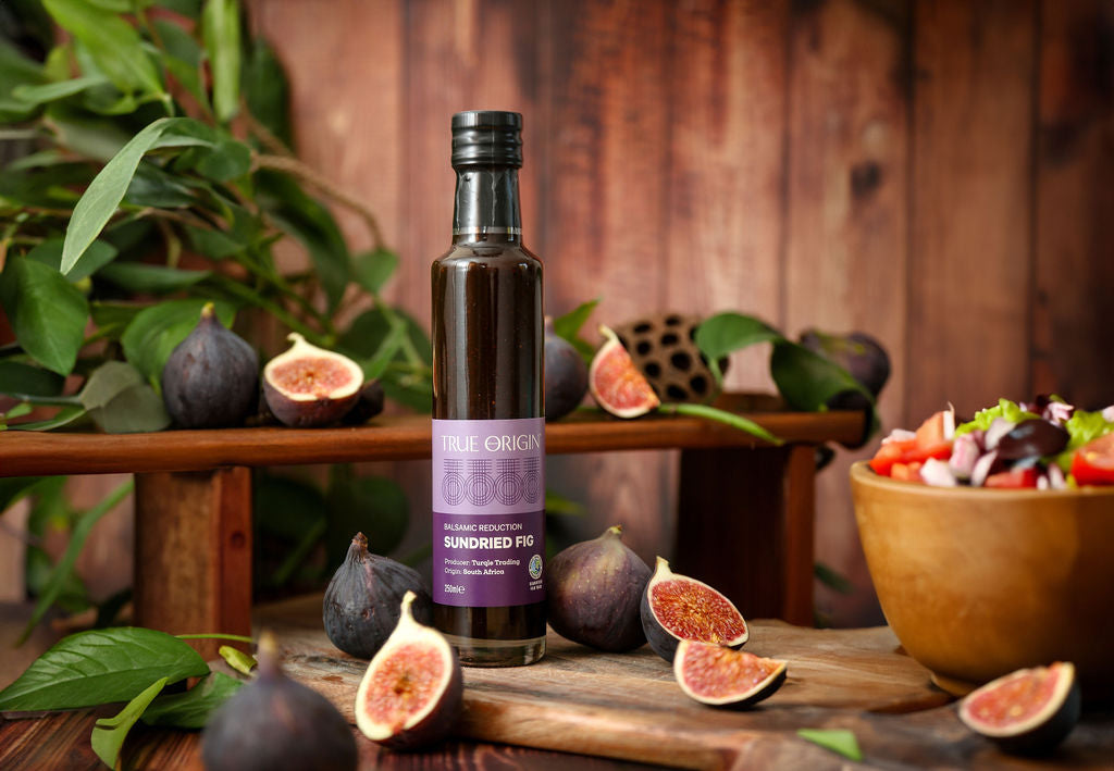 Bottle of sundried fig balsamic reduction on a wooden table with fresh figs and salad