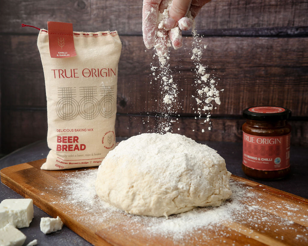 A bag of chilli and garlic beer bread next to some beer bread dough with flour being sprinkled over it.