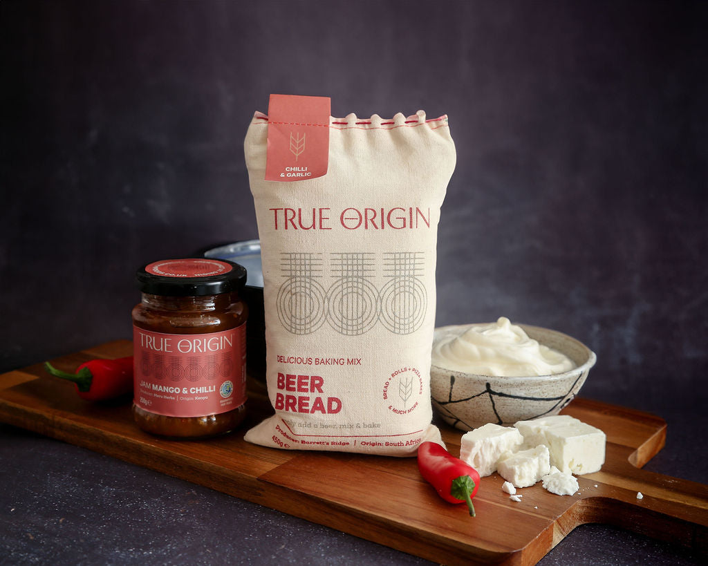 A bag of chilli and garlic beer bread next to a jar of mango and chilli jam and some fresh chillies and garlic.
