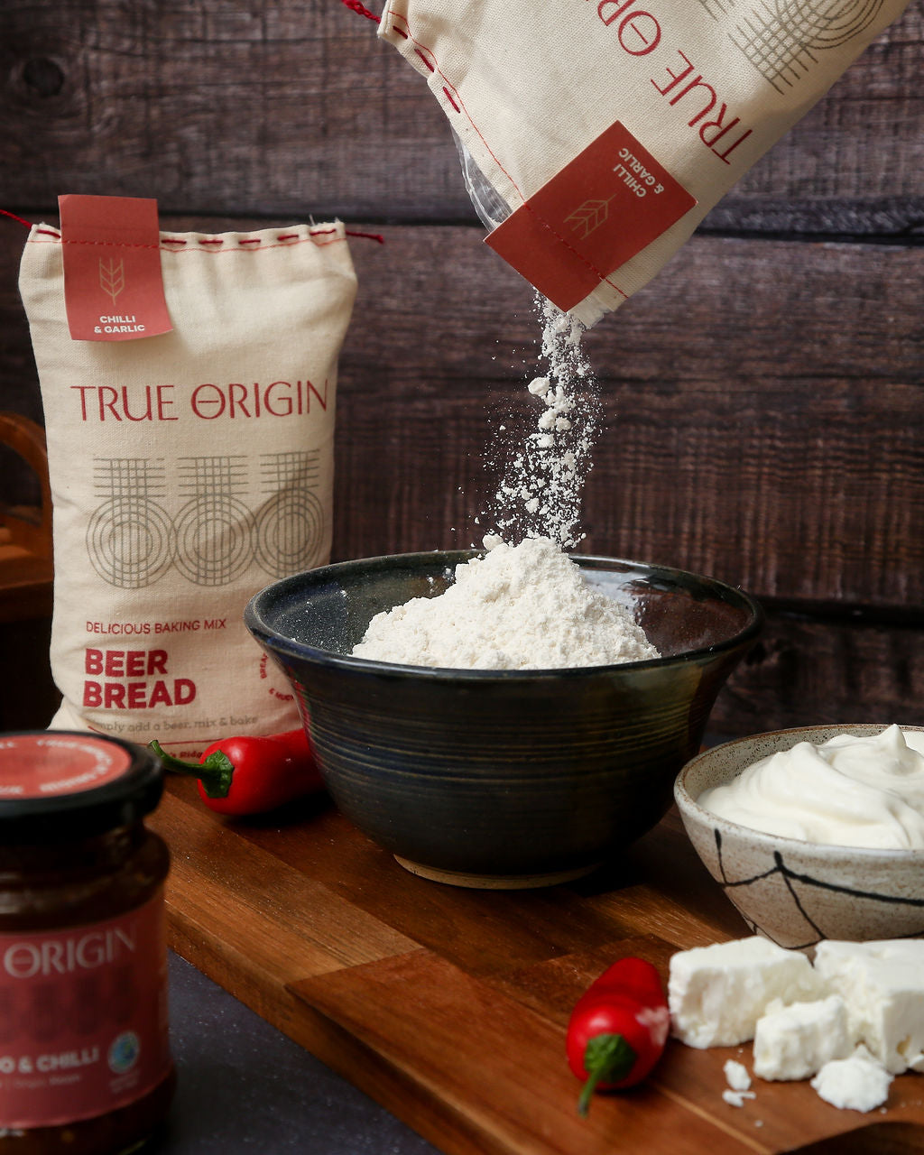 A bag of chilli and garlic beer bread next to a jar of mango and chilli jam and some fresh chillies and garlic.