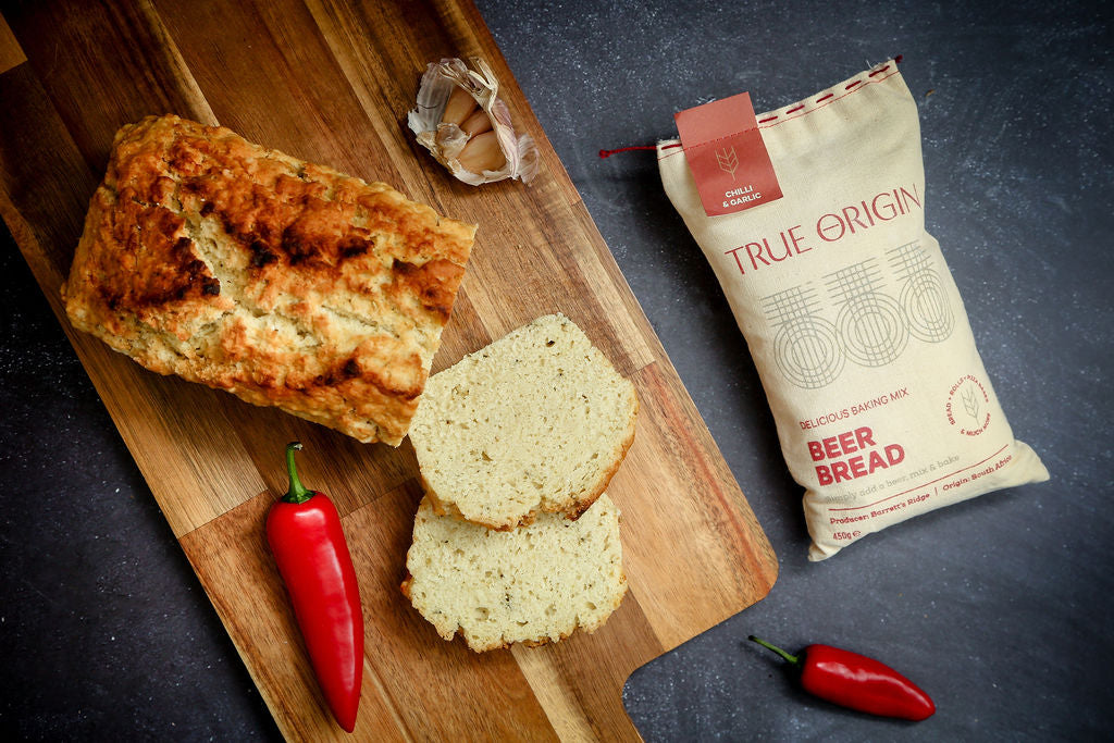 A bag of chilli and garlic beer bread next to a baked loaf of beer bread next to some fresh chillies and garlic.