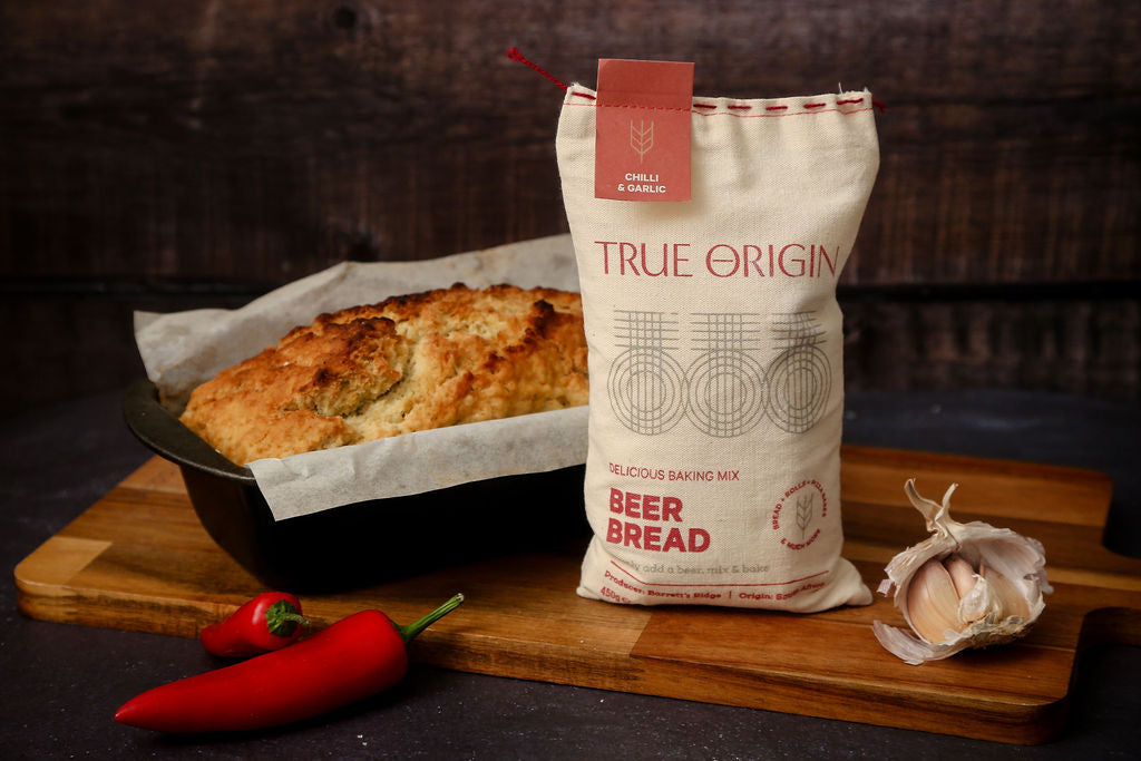 A bag of chilli and garlic beer bread next to a baked loaf of beer bread next to some fresh chillies and garlic.