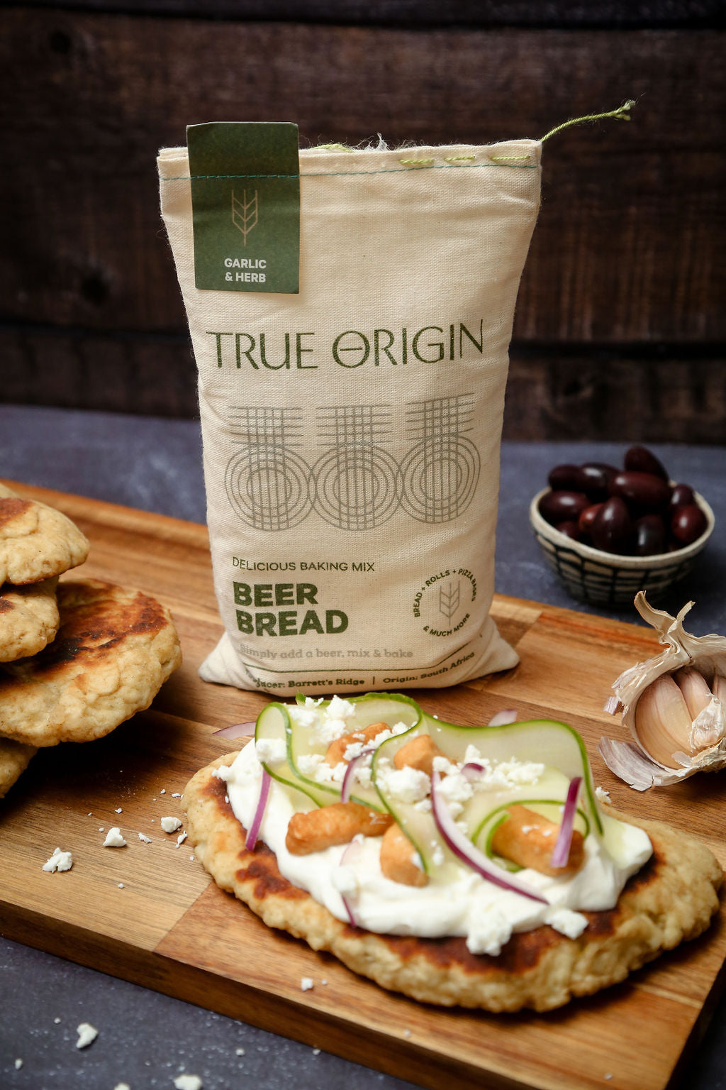A bag of True Origin Garlic & Herb Beer Bread on a wooden chopping board with a flatbread made out of garlic and herb beer bread.