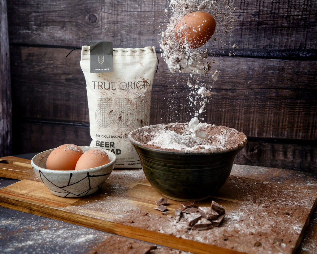 A bag of chocolate  and choc chip beer bread next a bowl of eggs and some beer bread mix and eggs being poured into a bowl.