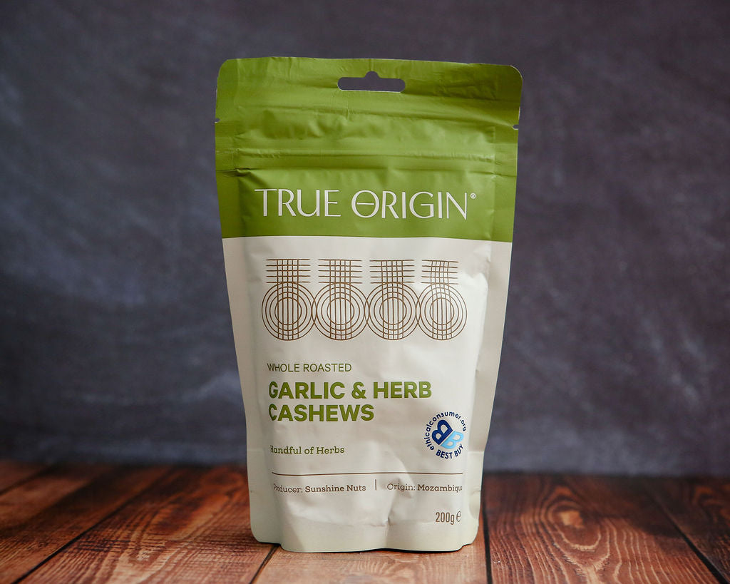 True Origin garlic and herb cashews package on a wooden surface with a dark background