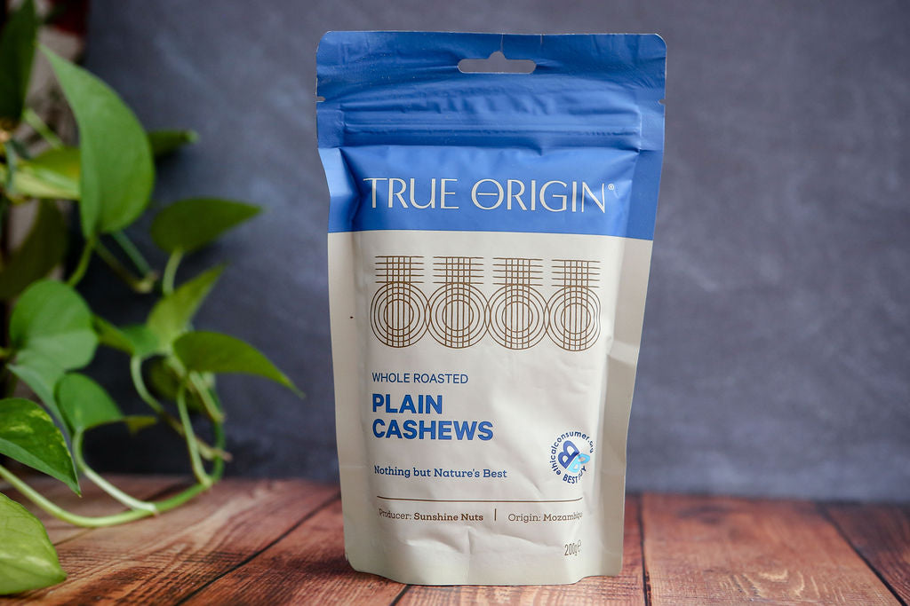 True Origin plain cashews packaging on a wooden surface with a plant in the background