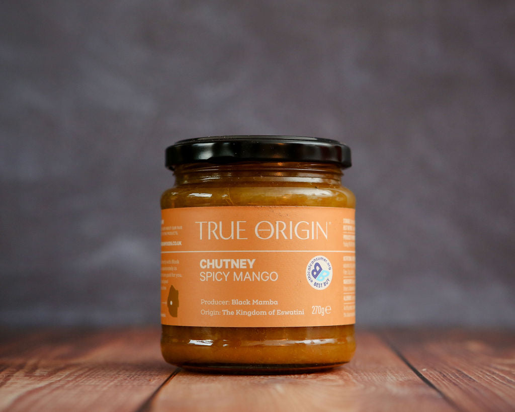 Jar of True Origin Spicy Mango Chutney on a wooden surface with a dark background