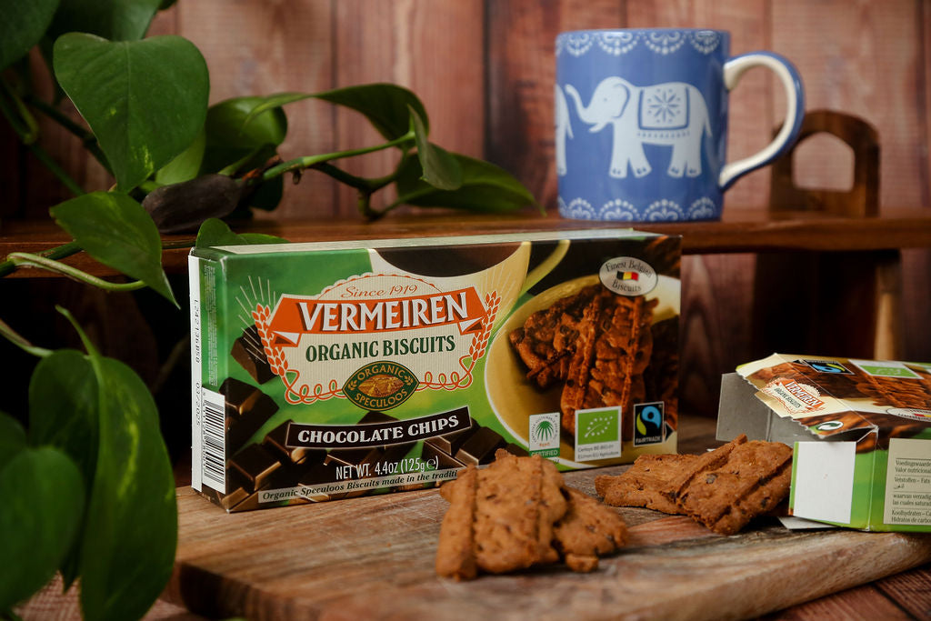 A packet of Fairtrade Vermeiren organic choc chip biscuits from Belgium next to an open packet with some loose biscuits falling out and a cup of tea ready for dunking. 