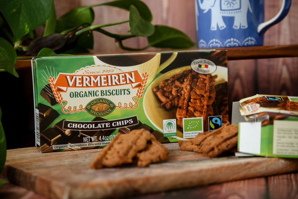 A packet of Fairtrade Vermeiren organic choc chip biscuits from Belgium next to an open packet with some loose biscuits falling out and a cup of tea ready for dunking. 