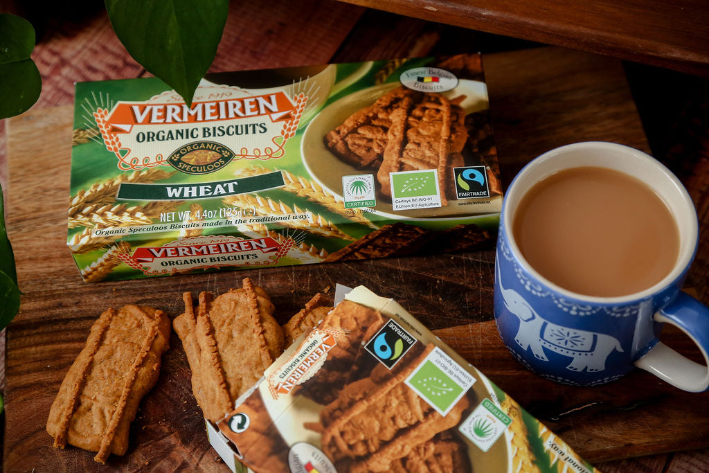 A packet of Fairtrade Vermeiren organic wheat biscuits from Belgium next to an open packet with some loose biscuits falling out and a cup of tea ready for dunking. 