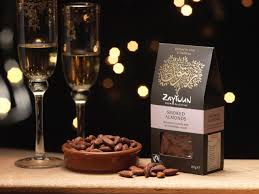 Two flute glasses of champagne with a bowl of smoked almonds and a box of Fairtrade Zaytoun smoked almonds from Palestine.