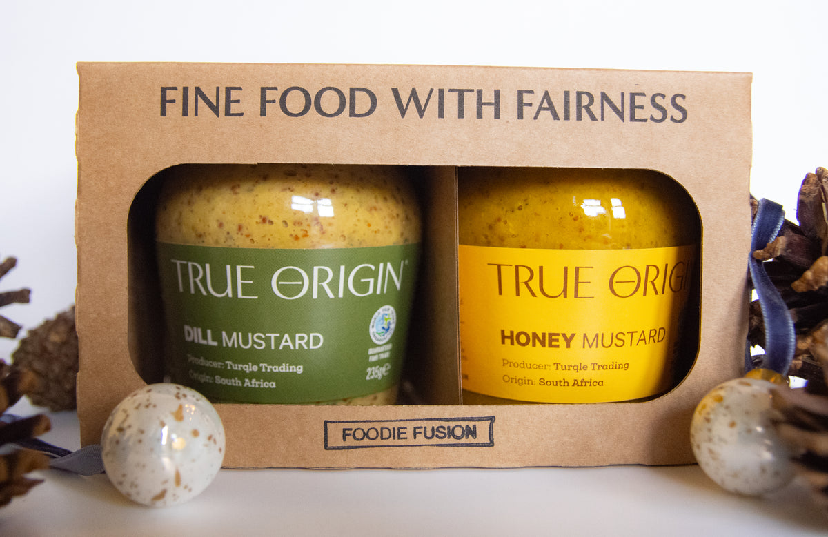 A gift set of two mustard jars in a brown cardboard box. The left jar is labeled 'TRUE ORIGIN DILL MUSTARD' in green, and the right jar is labeled 'TRUE ORIGIN HONEY MUSTARD' in yellow.