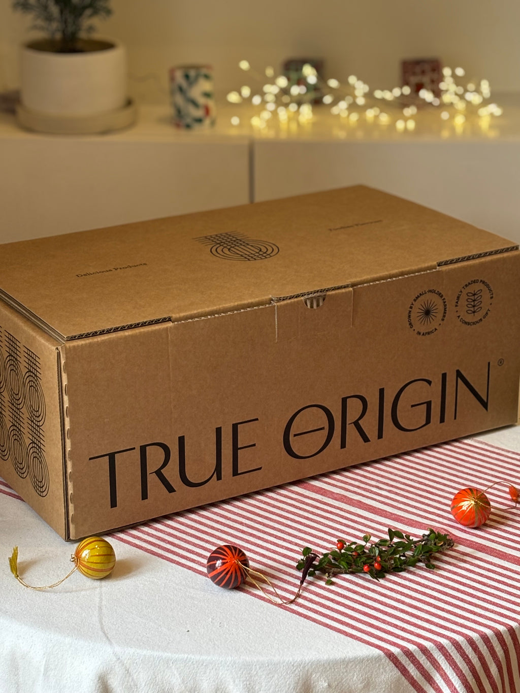 Cardboard hamper box with 'True Origin' branding on a table with decorative items.