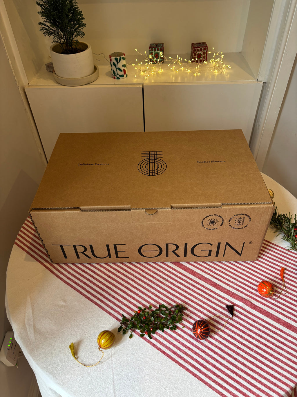Cardboard hamper box labeled 'True Origin' on a table with Christmas decorations.