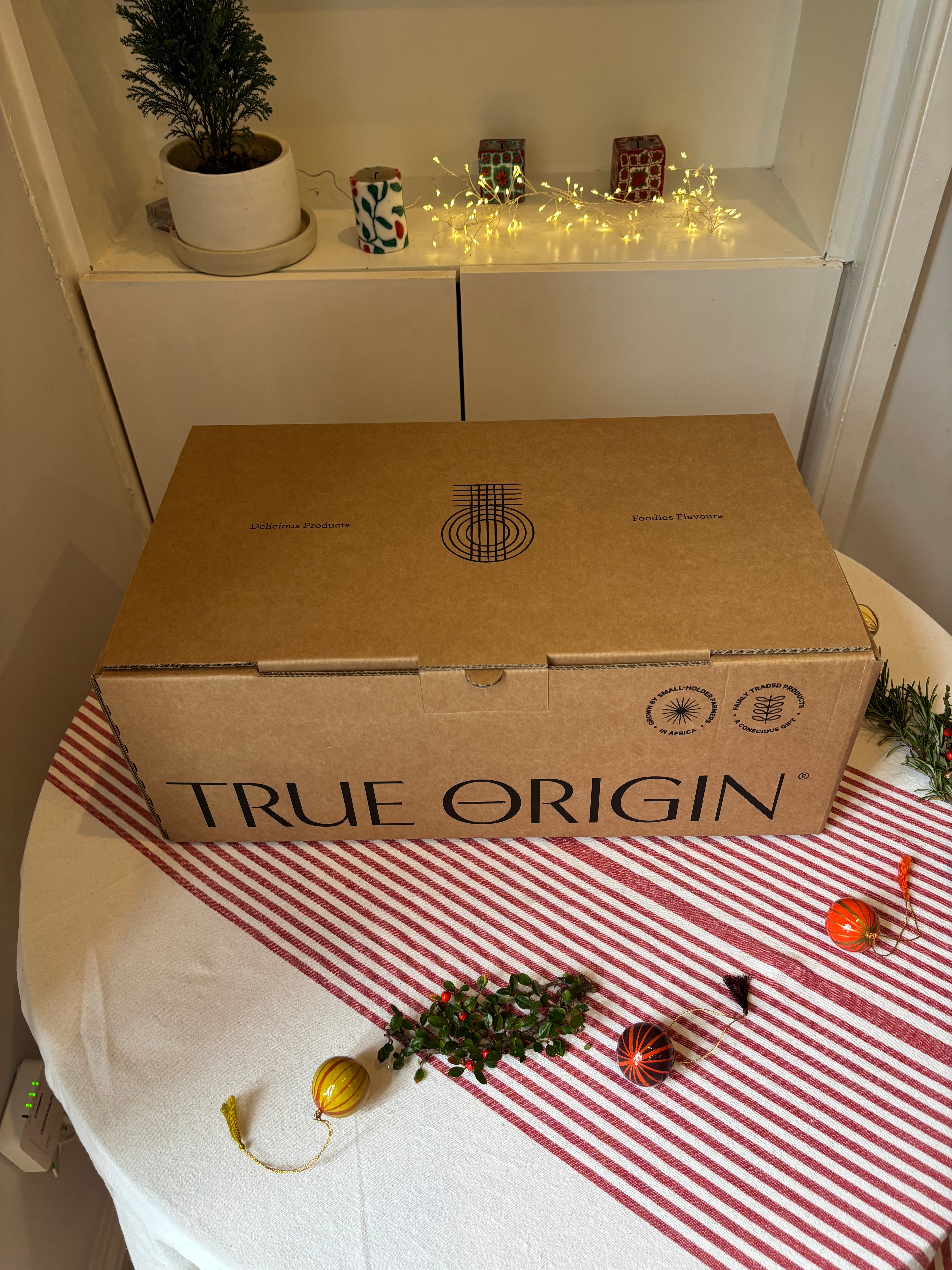 Cardboard hamper box labeled 'True Origin' on a table with Christmas decorations.