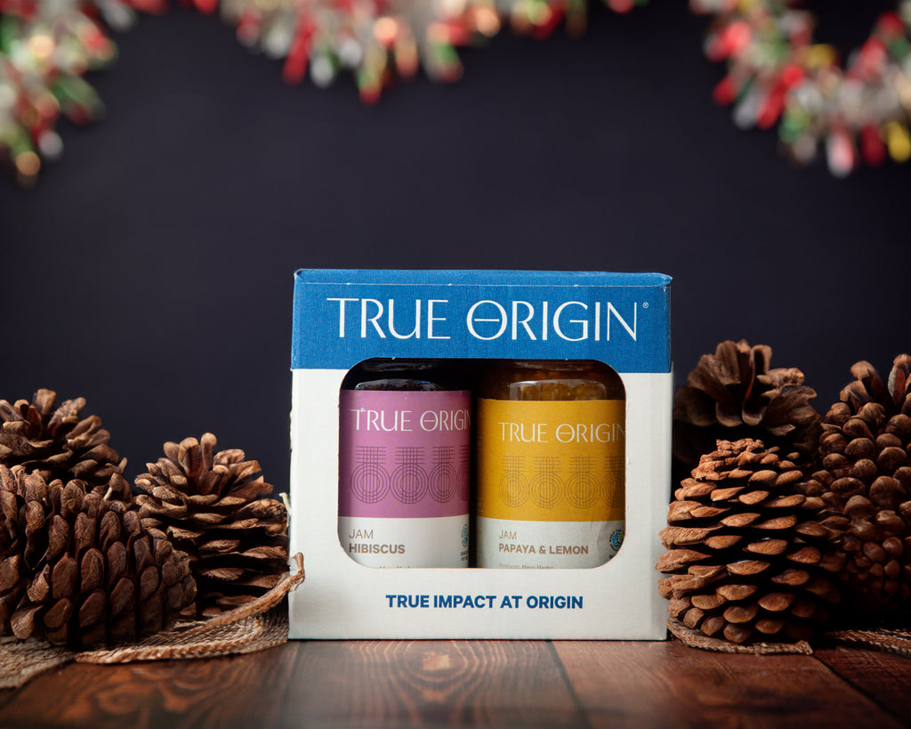 A True Origin branded tropical duo gift set containing Papaya & Lemon Jam and Hibiscus Jam.  Pine cones are placed beside the gift set and there is tinsel hanging in the background to depict the suitability for a christmas gift.
