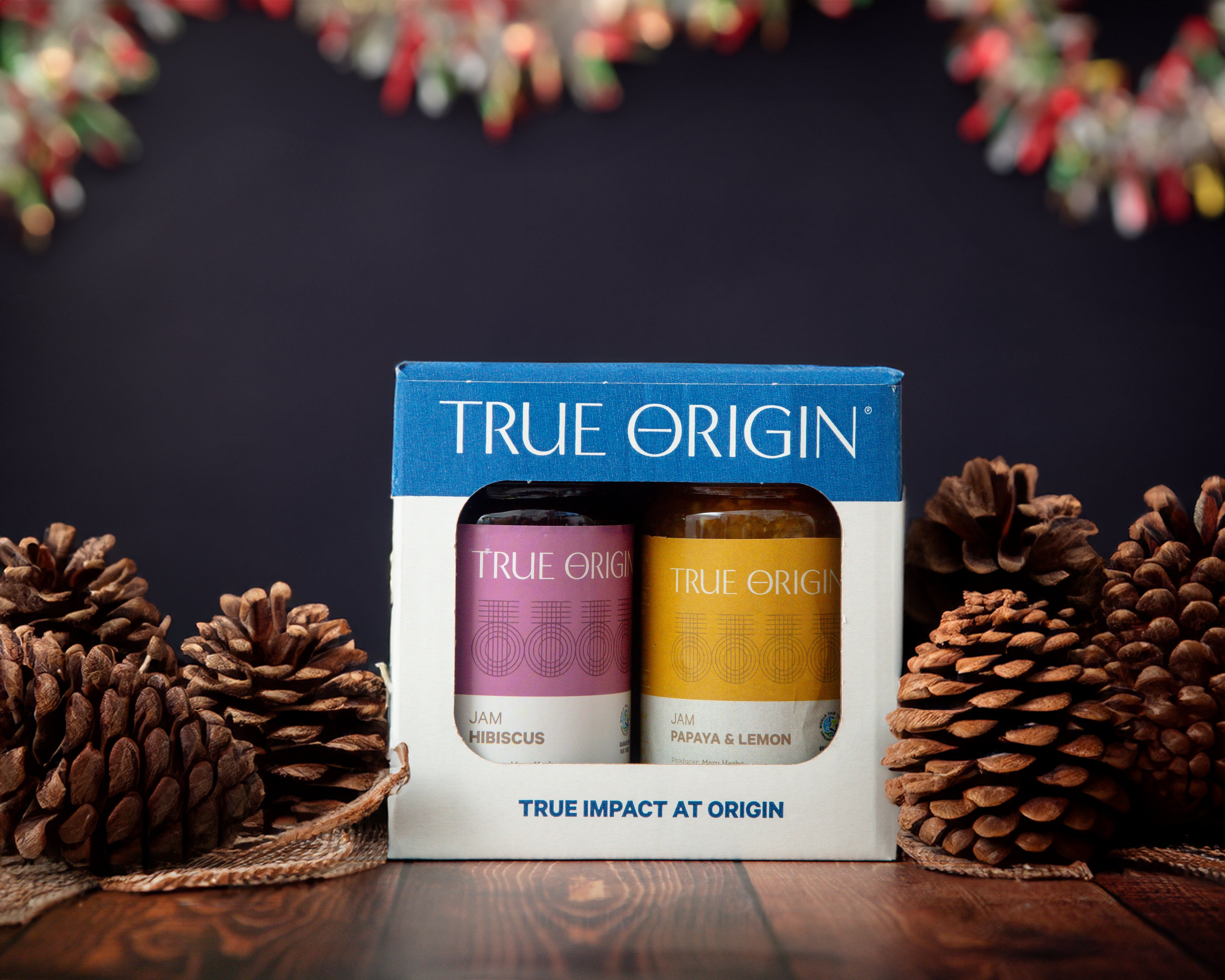 A True Origin branded tropical duo gift set containing Papaya & Lemon Jam and Hibiscus Jam.  Pine cones are placed beside the gift set and there is tinsel hanging in the background to depict the suitability for a christmas gift.