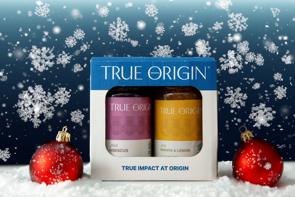 A True Origin branded tropical duo gift set containing Papaya & Lemon Jam and Hibiscus Jam.  It is sitting in some snow with a red bauble either side and a dark blue background with lots of snowflakes.