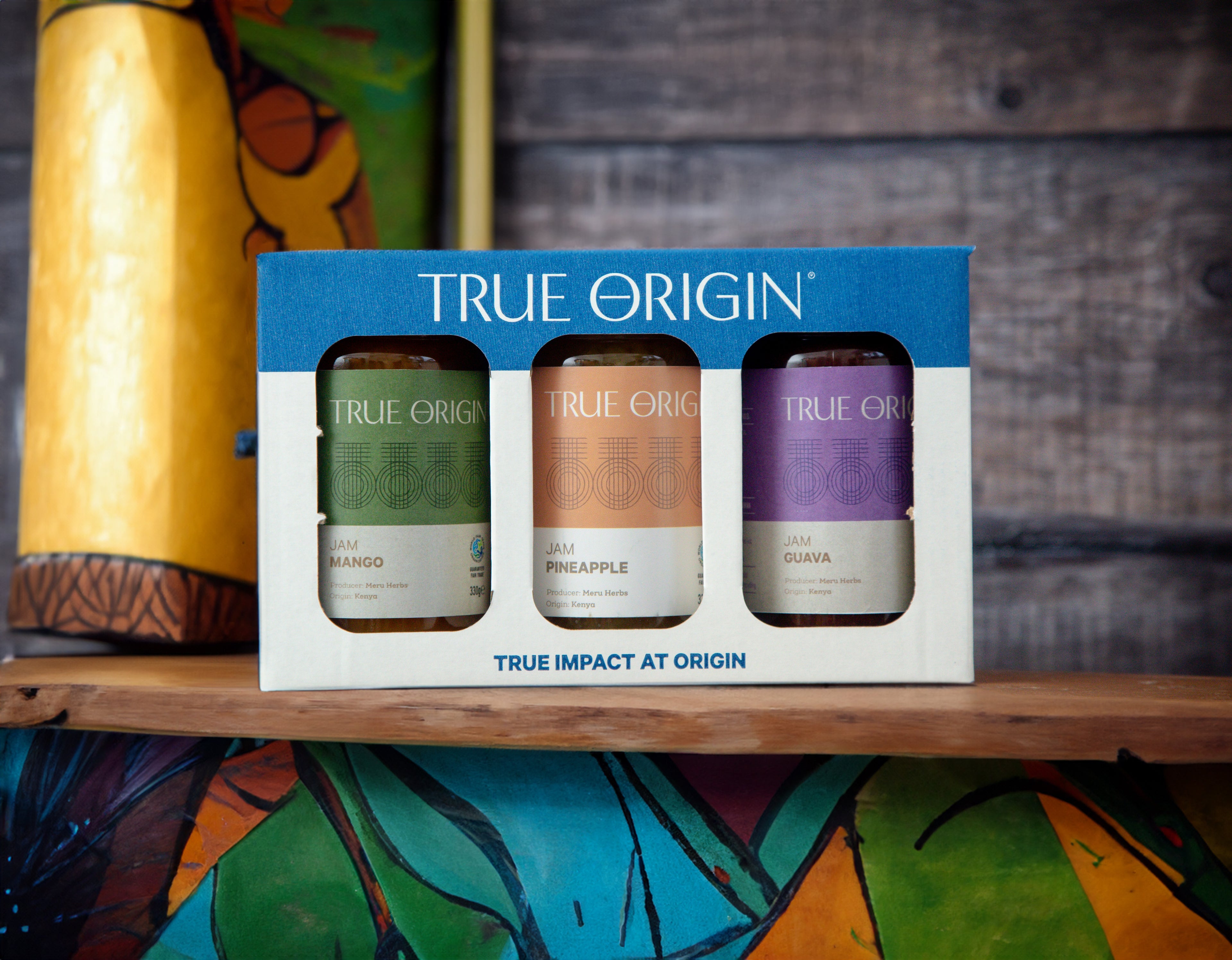 A gift set box containing three jars of True Origin brand jams: Guava Jam, Pineapple Jam, and Mango Jam, each with a clear label showing the flavour and 'True Impact at Origin' text.