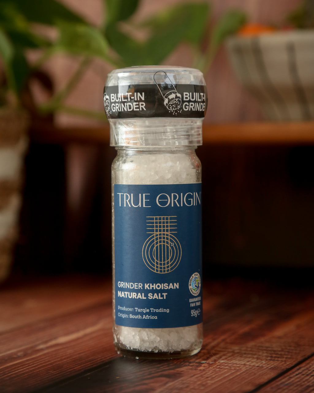 A clear glass bottle with a built-in grinder containing natural Khoisan salt, labelled 'True Origin'.