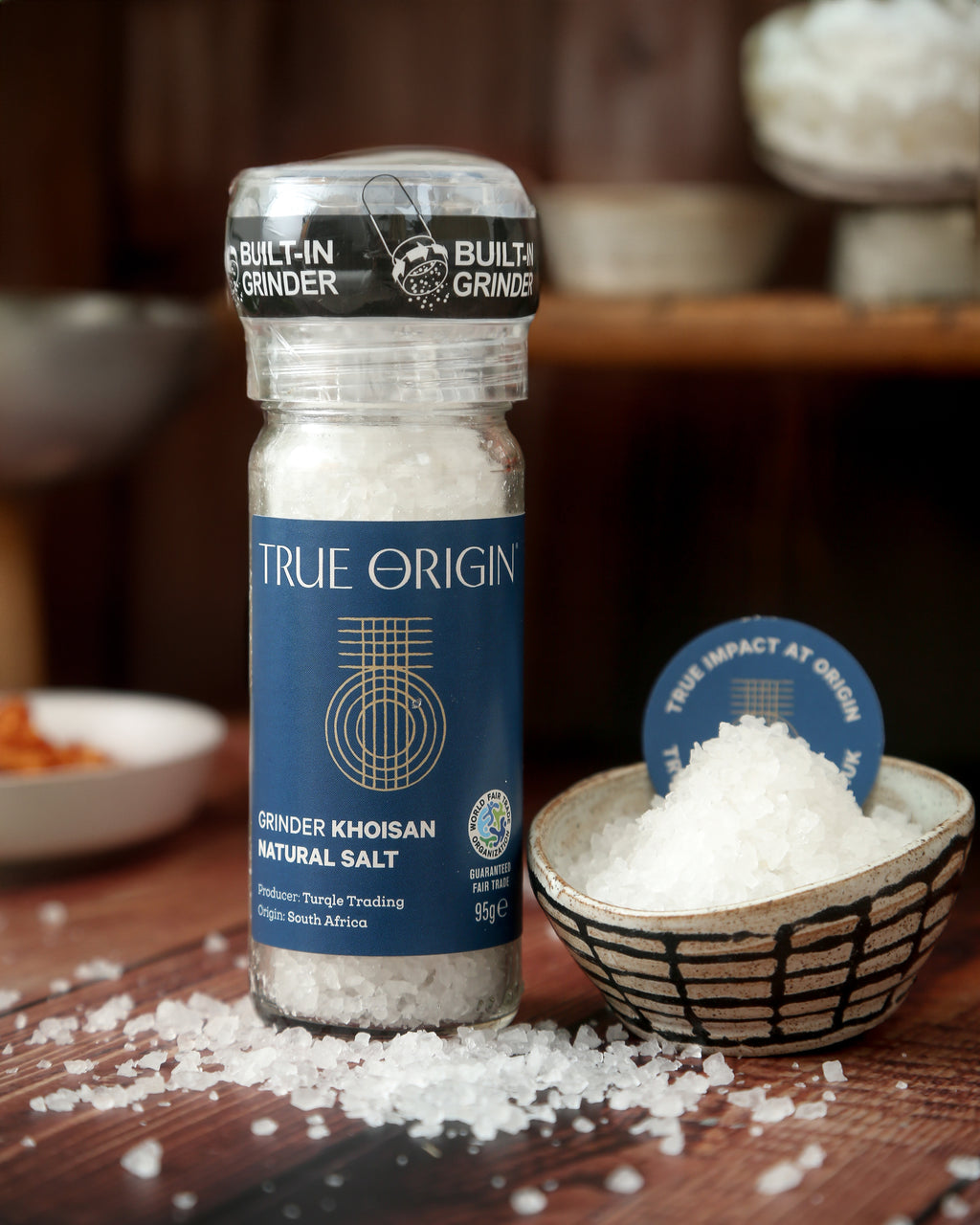 A clear glass bottle with a built-in grinder containing natural Khoisan salt, labelled 'True Origin'.