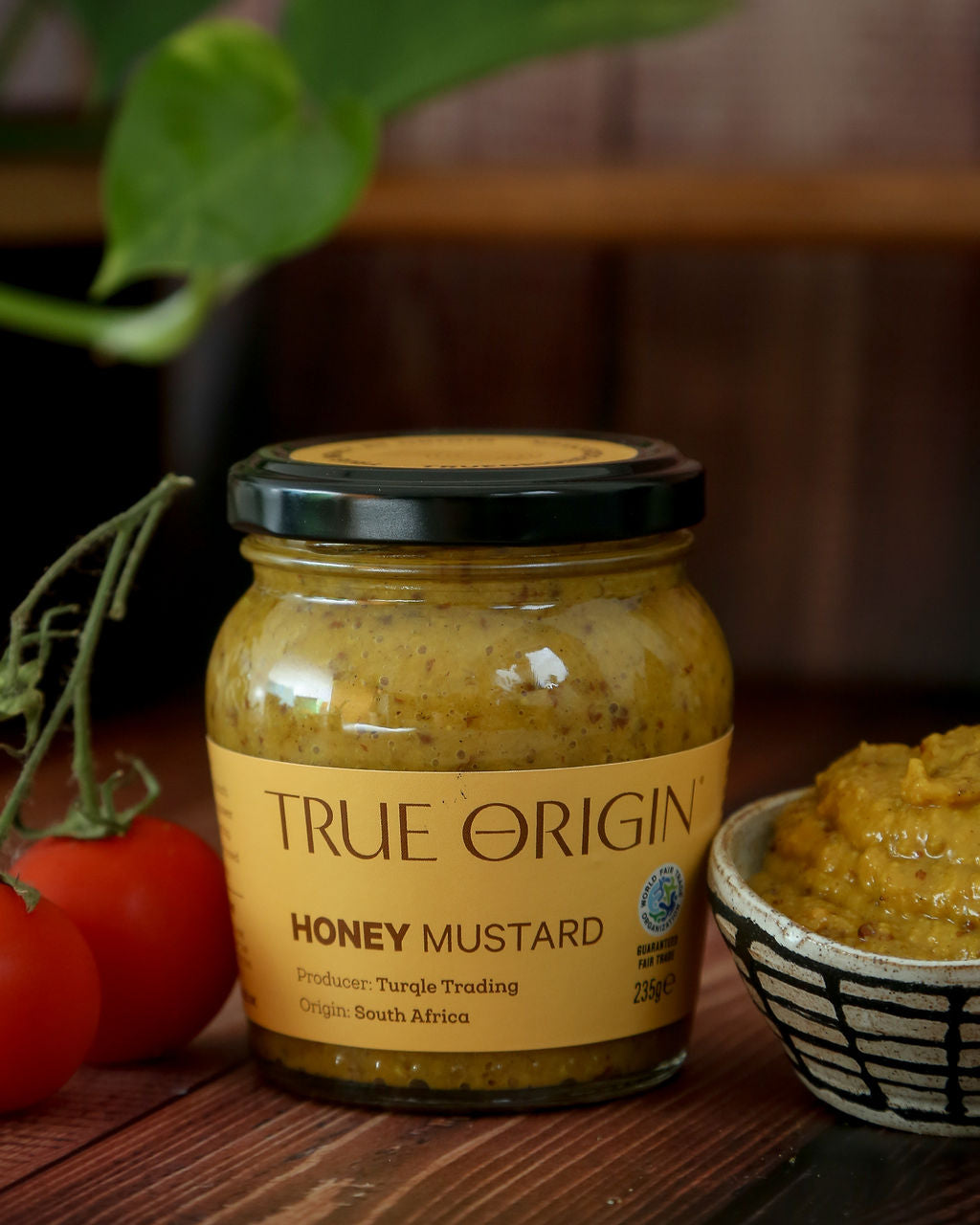 A jar of True Origin fair trade Honey Mustard from South Africa next to a bowl containing the yellow mustard.