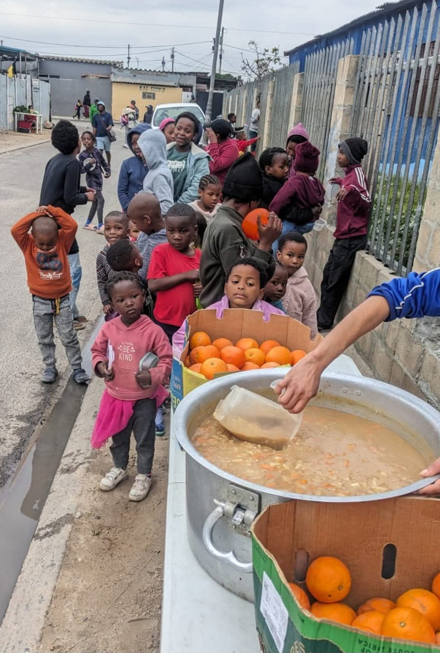 Children gathered around a pot of soup with oranges on a street. This is Ukama Foundation Souperheros