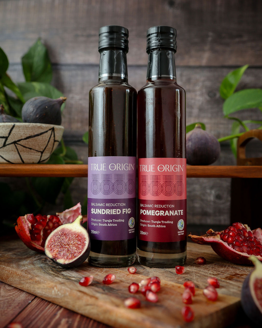 Image of True Origin fair trade Sundried Fig and Pomegranate Balsamic Reductions on a chopping board with figs and pomegranate seeds.