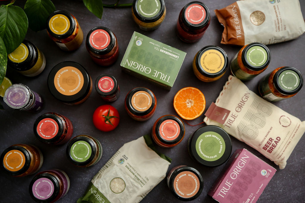 Collection of small bottles and packages with 'True Origin' branding on a dark surface.