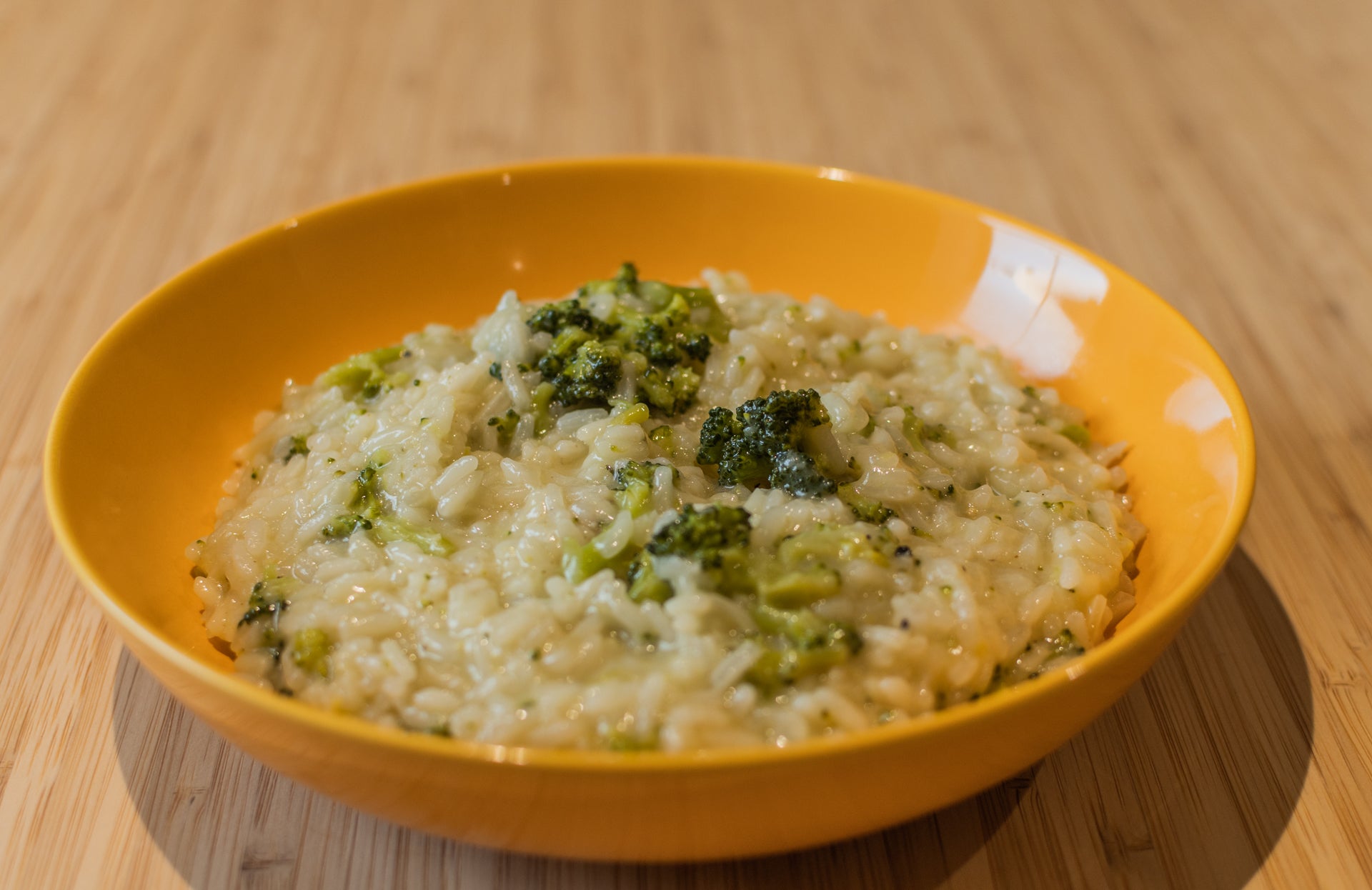 A yellow bowl with some freshly cooked broccoli and lemon risotto using Kilombero rice.