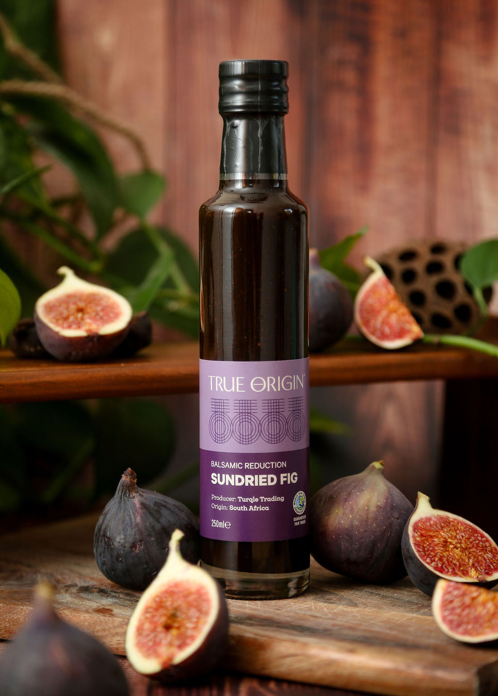 A purple bottle of sundried fig balsamic reduction surrounded by figs on a wooden chopping board.