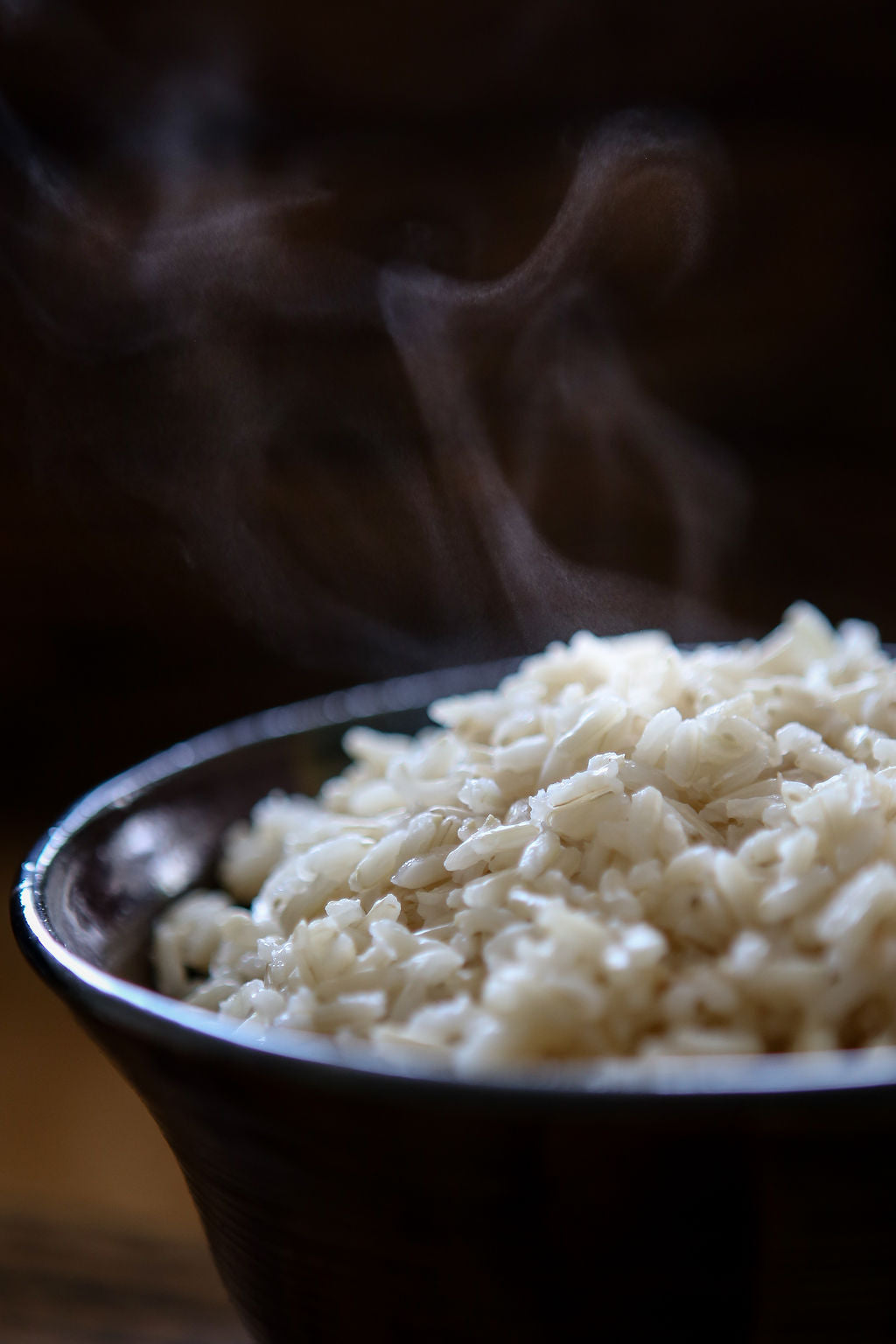 A bowl of freshly cooked steaming hot white Kilombero rice with a dark background.