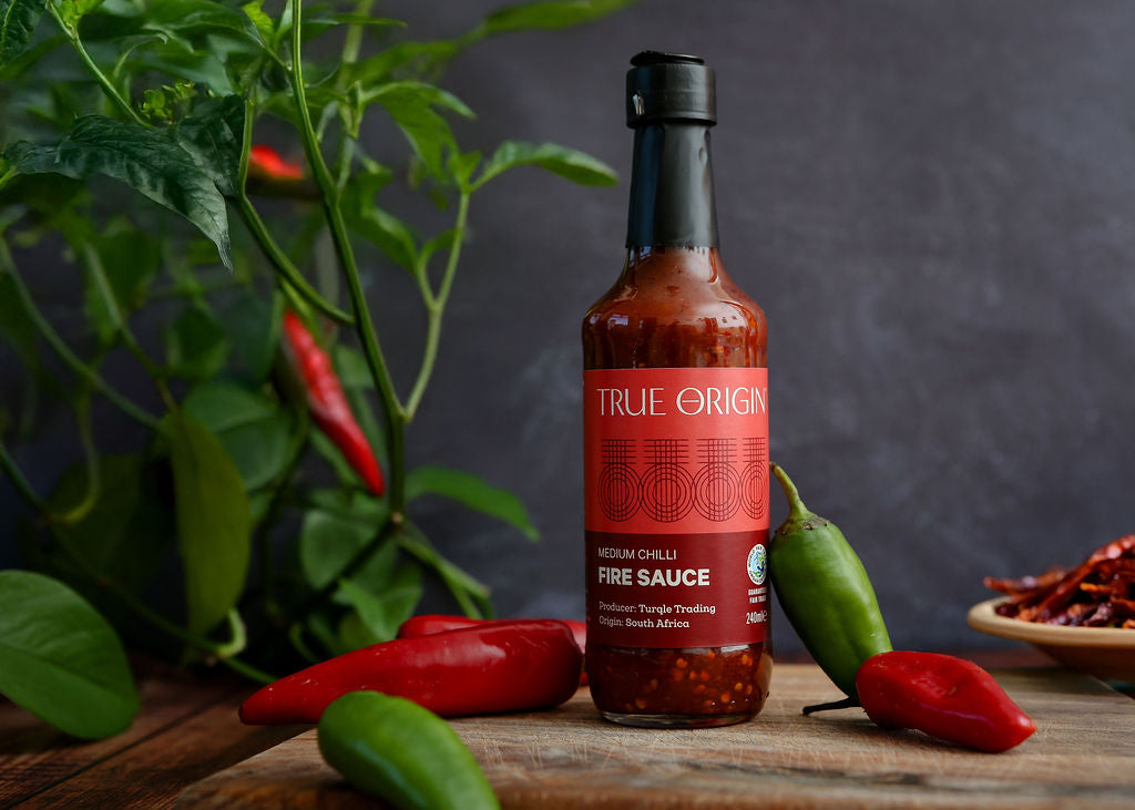 Bottle of True Origin fire sauce with chili peppers on a wooden surface