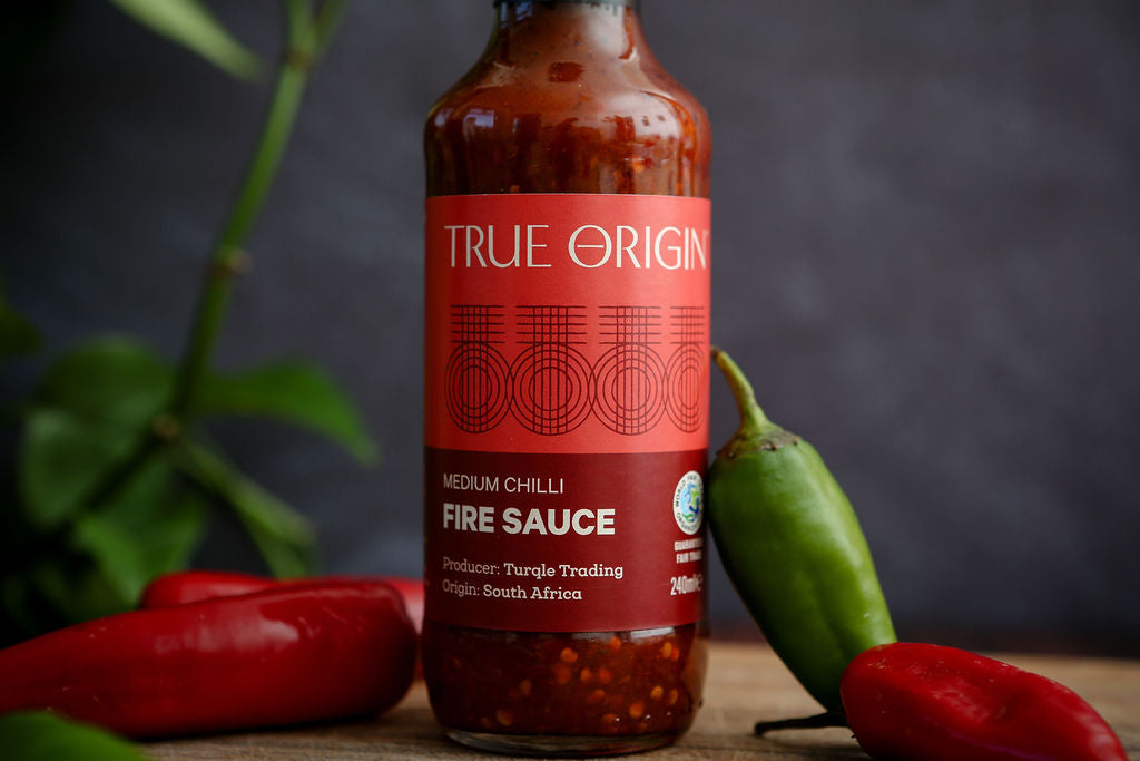 Bottle of True Origin fire sauce with peppers on a wooden surface