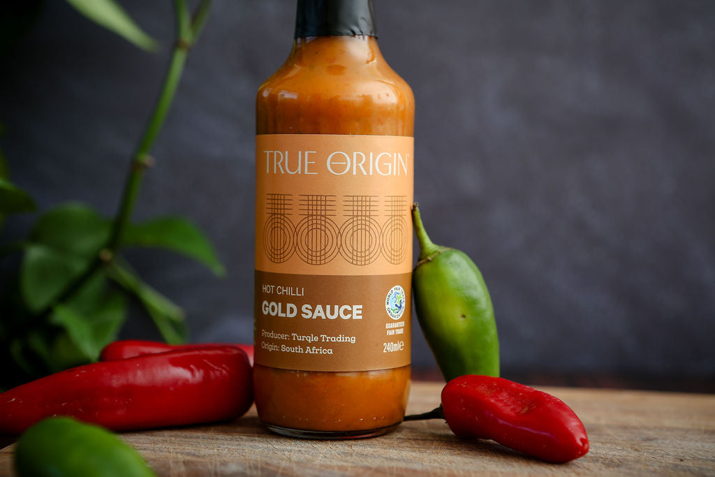 True Origin hot chili gold sauce bottle with peppers on a wooden surface
