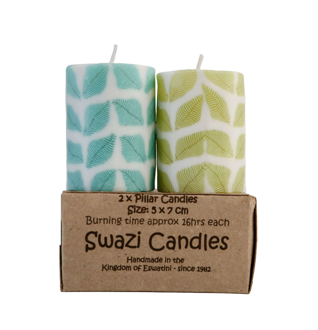Two pillar candles with leaf patterns in a cardboard box labeled 'Swazi Candles'.