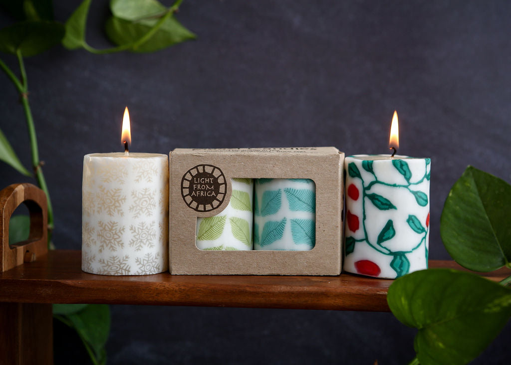Four candles with different designs in front of a cardboard box labelled 'Light from Africa' on a wooden surface.