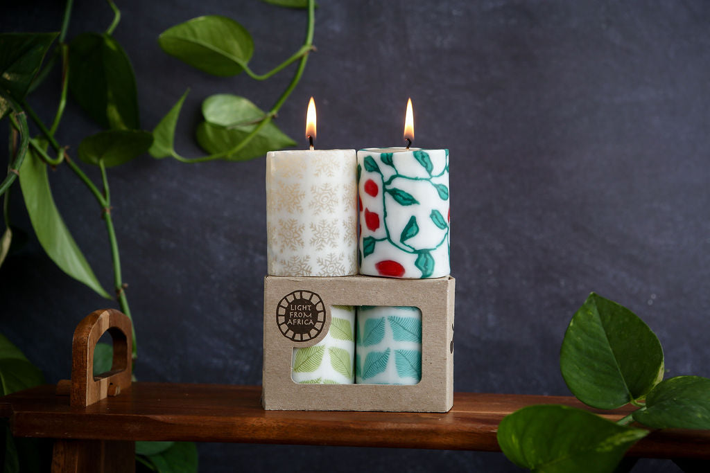 Two candles in a box and two candles sitting on top of the box with a plant in the background
