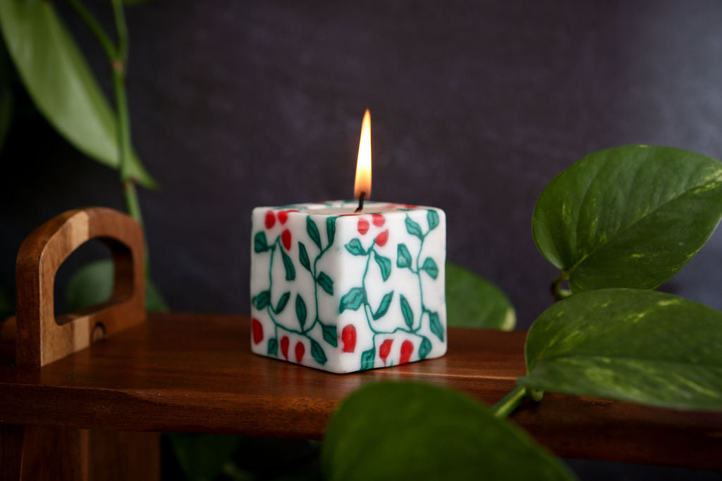 Candle with festive holly design on a wooden surface with leaves in the background