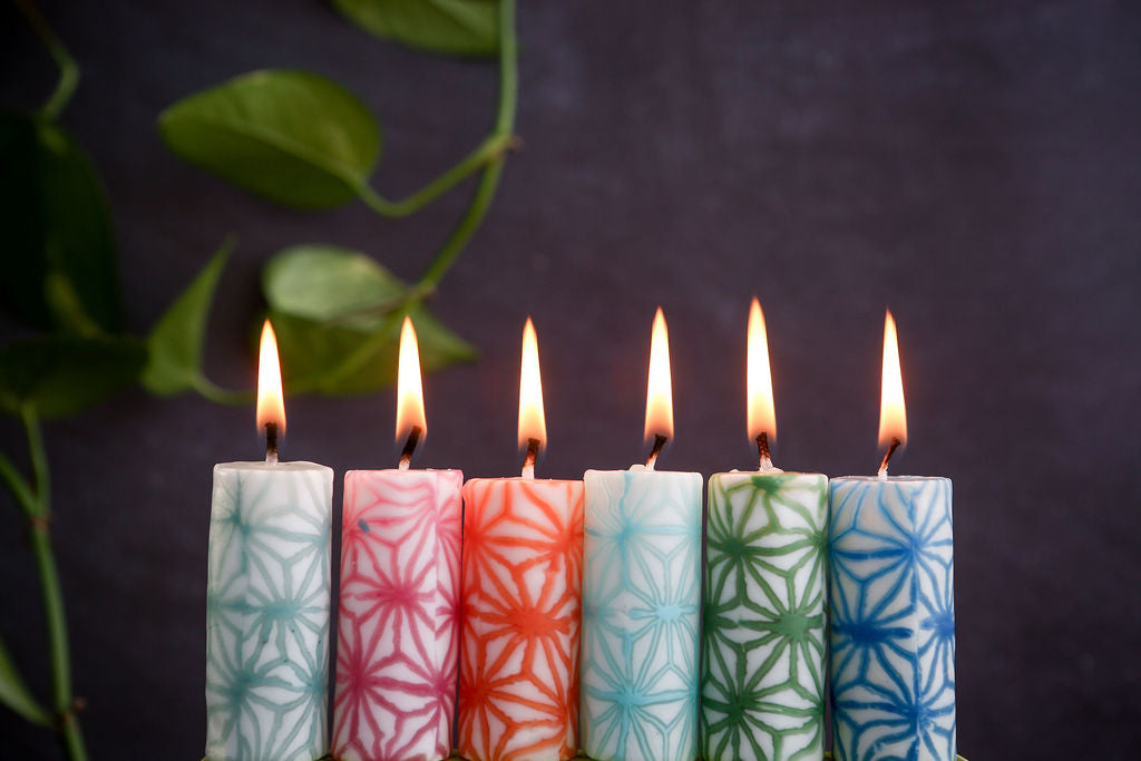 Six lit candles with colourful patterns on a dark background