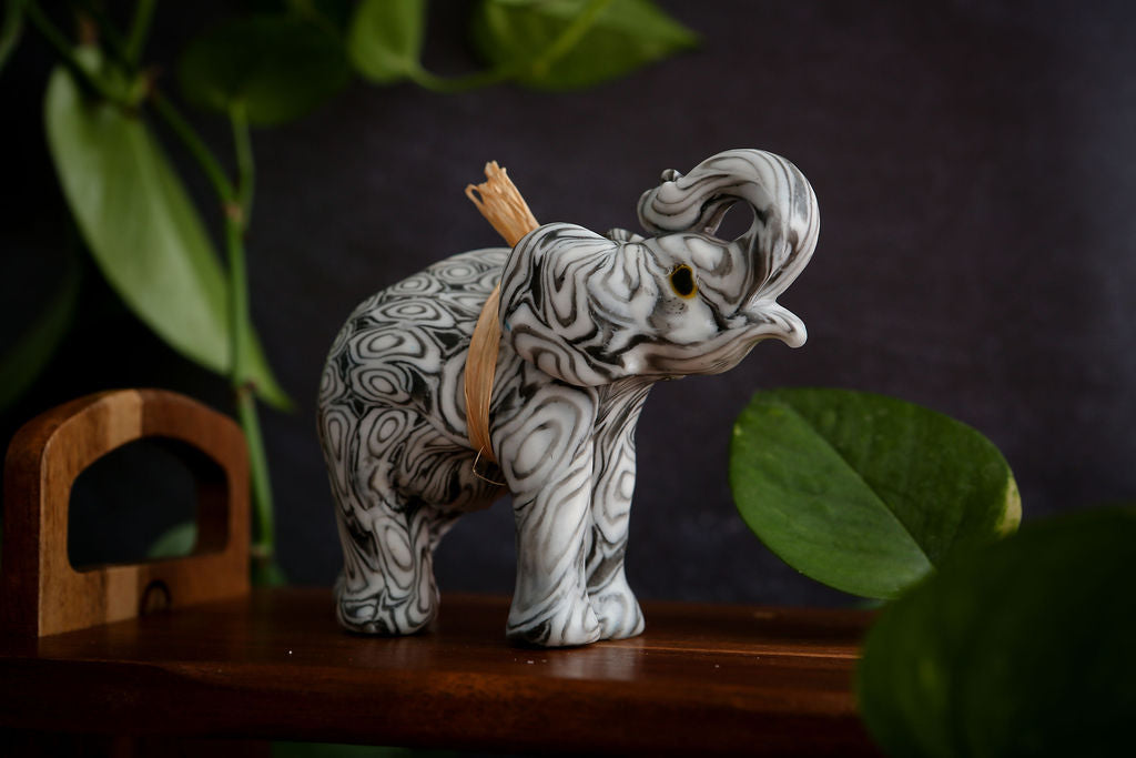Decorative elephant candle with intricate patterns on a wooden surface with green leaves in the background