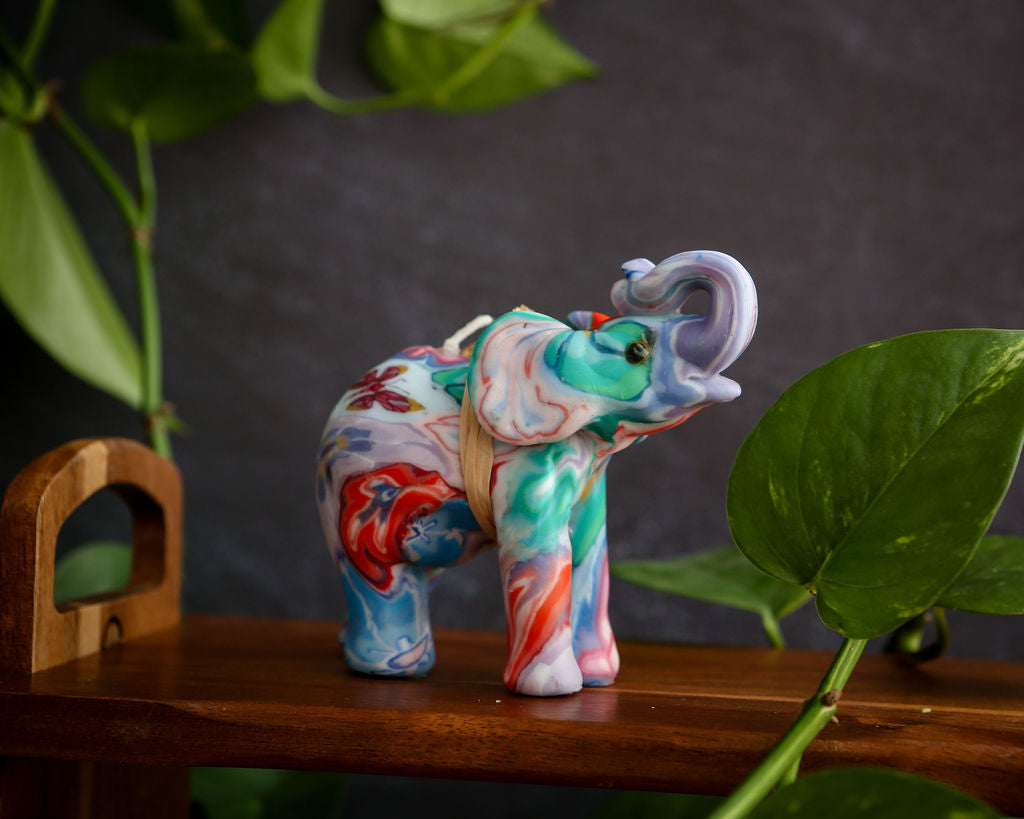 Colourful elephant candle on a wooden surface with green leaves in the background